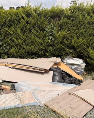 Before: boards and panels from a ripped out kitchen, with roofing sheets and bin bags, piled by a hedge
